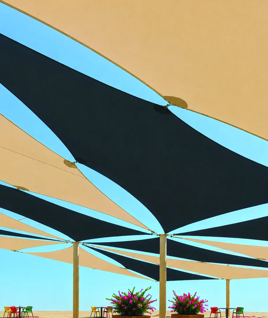Voiles d'ombrage beiges et anthracite tendues au-dessus d'une terrasse sous un ciel bleu